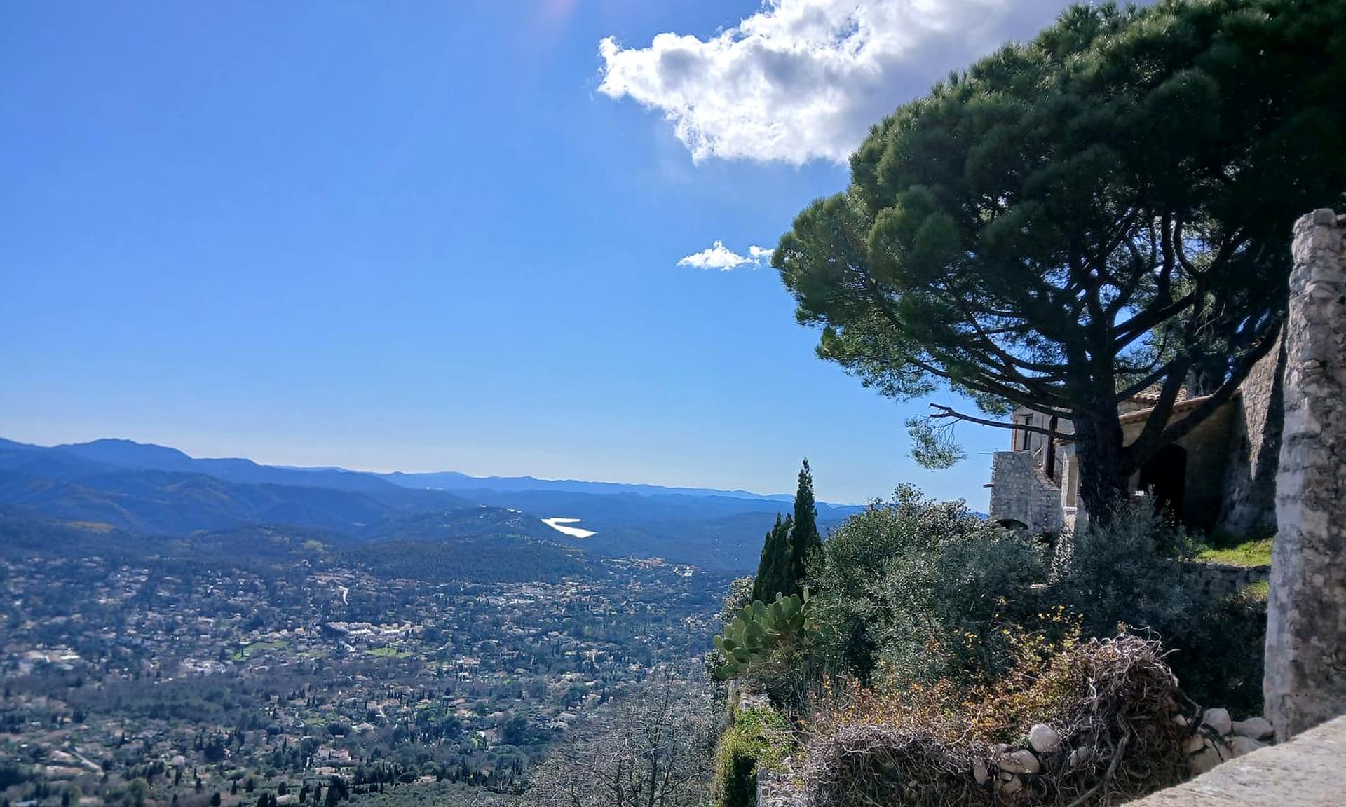 Vista do alto sobre o vale, com casa de pedra e pinheiro, no passeio por Cabris, Gourdon e Grasse.